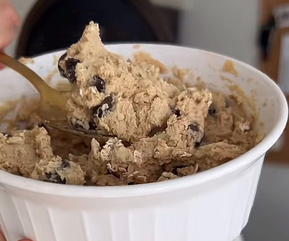 A spoonful of chocolate-chip dough above a white bowl